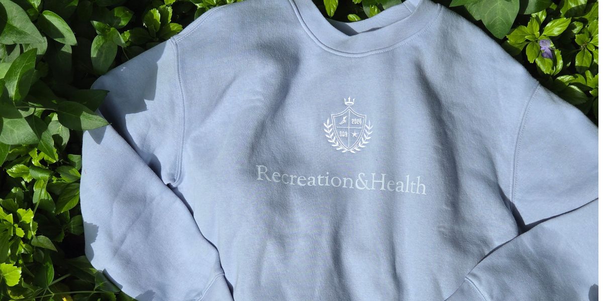 Picture of a light blue crewneck sweatshirt laying in green foliage.