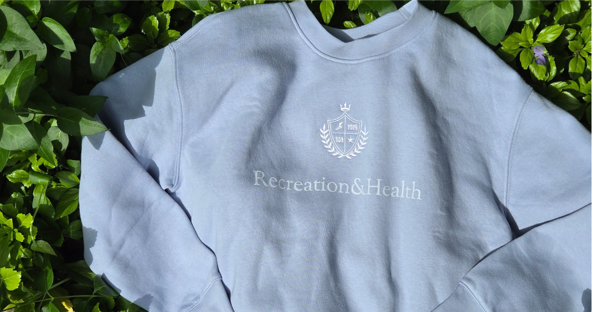 Picture of a light blue crewneck sweatshirt laying in green foliage.