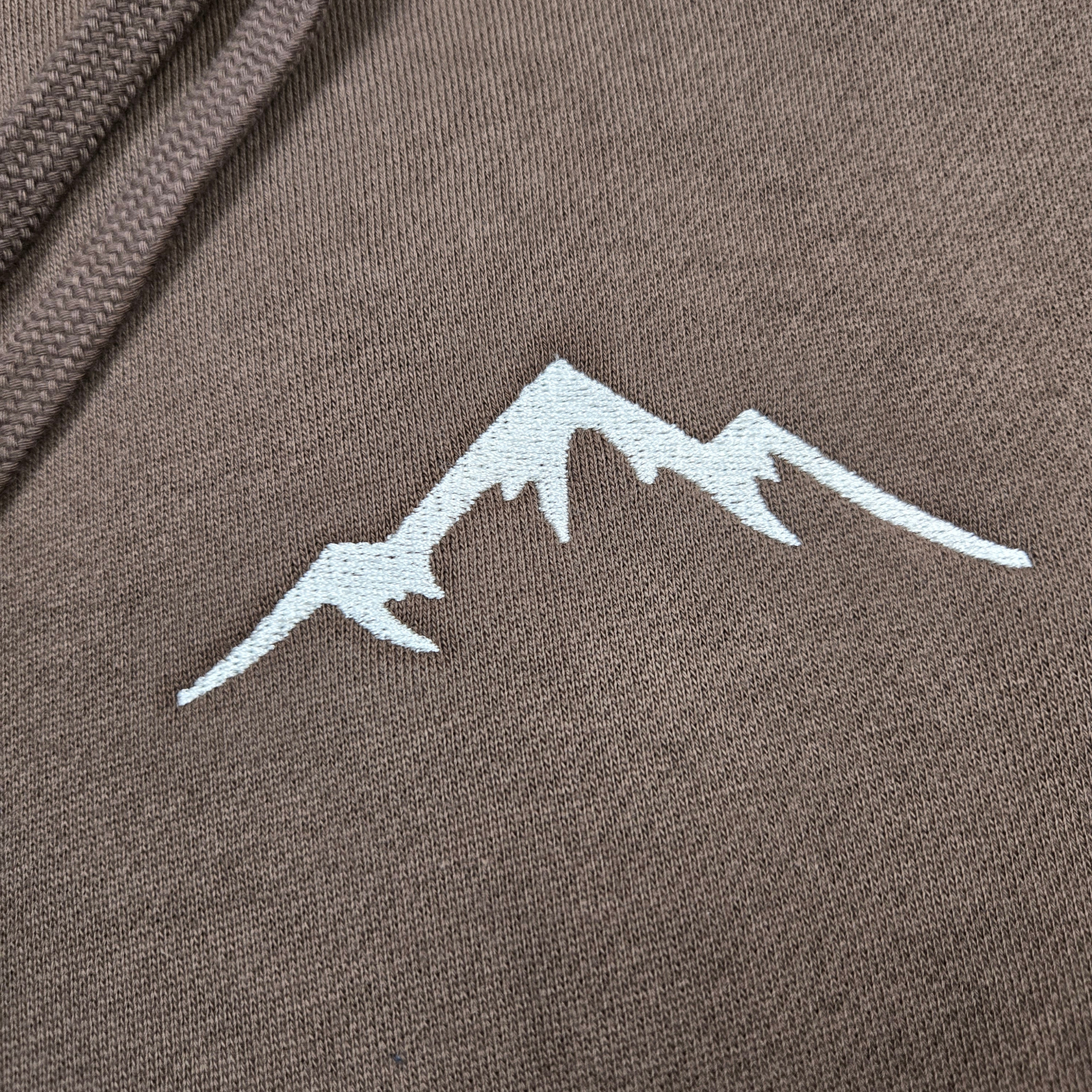 closeup of swith backcountry ski club fleece hoodie with mountain logo embroidered in off-white on a brown cotton-blend fabric 