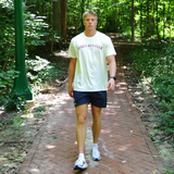 Athletic man walking on a brick path in a forested area wearing swith apres run club crewneck tee and swith riviera collection swim short.