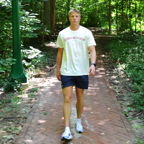 Athletic man walking on a brick path in a forested area wearing swith apres run club crewneck tee and swith riviera collection swim short.