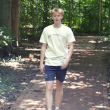 Athletic man wearing swith apres racquet club crewneck tee and swith riviera collection swim shorts walking on a brick path with greenery in the background