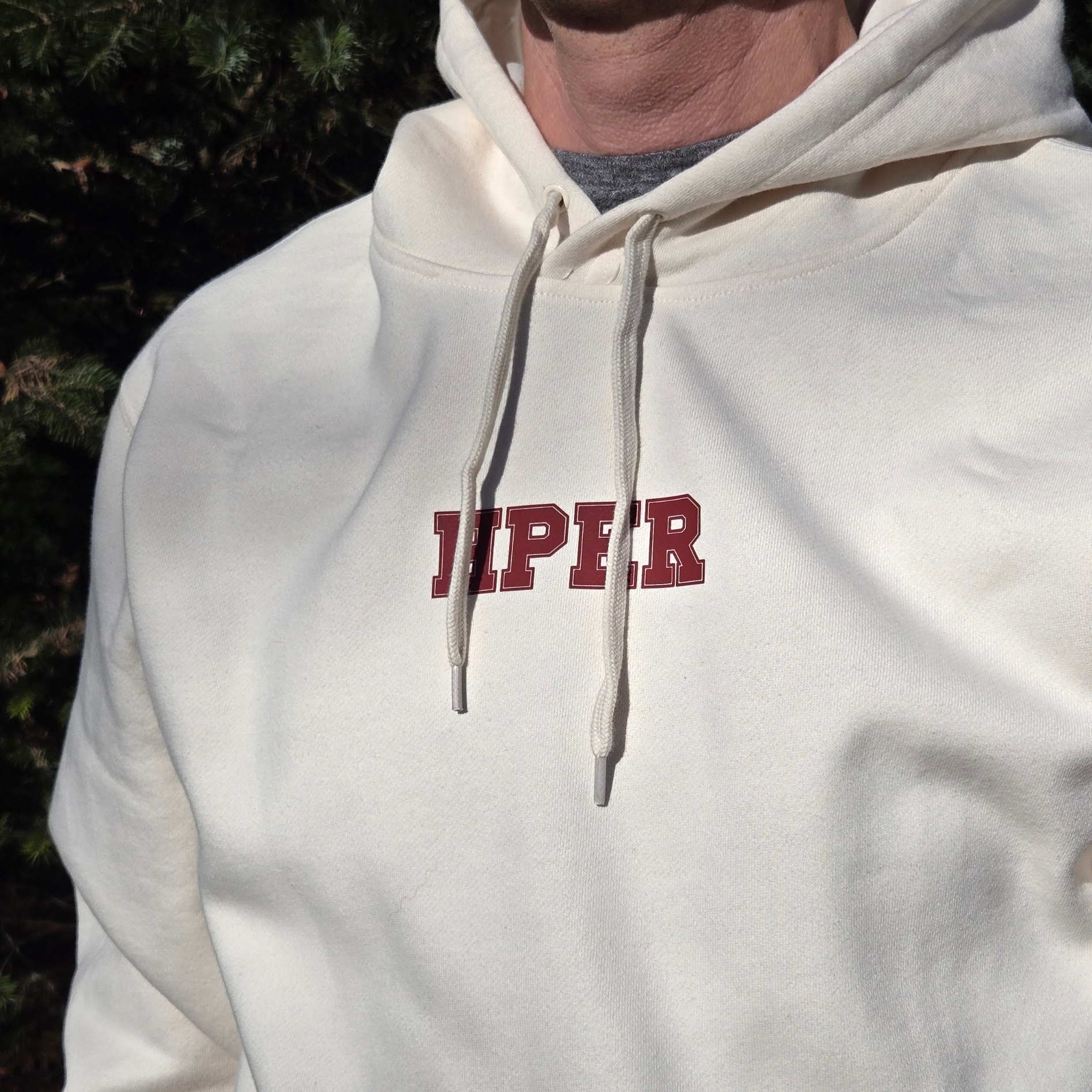 swith hper fleece hoodie in cream color with 'HPER' text in crimson color on a man outdoors